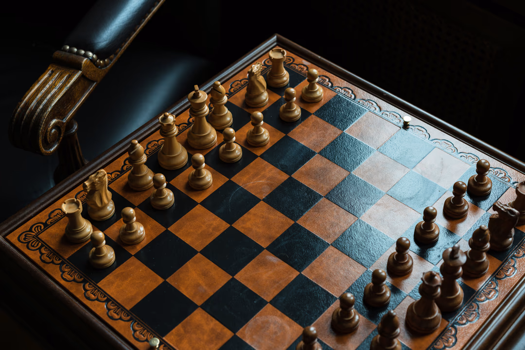 昏暗光線下的木製西洋棋盤與棋子，象徵多個 AI 代理人同場競爭時的賽局與協議關係