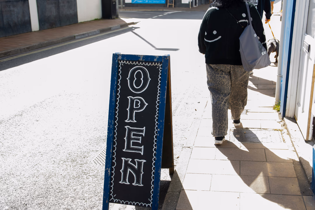 人行道上的 Open 營業立牌與經過的路人，象徵營業時間資訊是否正確