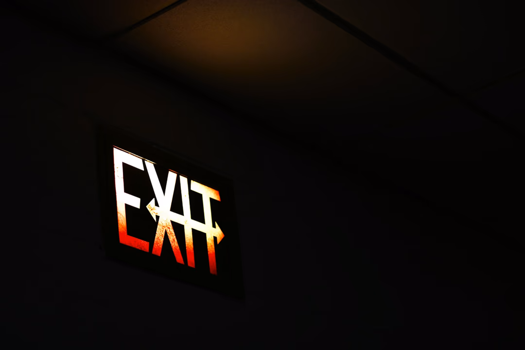 黑暗中亮著的 EXIT 出口指示燈，象徵資遣通知在法律上必須說清楚的那段過程