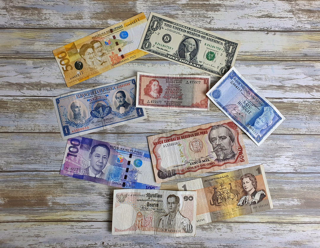 木紋桌上攤開多個國家的紙鈔，象徵公司同時持有與收受多種外幣時，每一種都有自己的匯率時間軸