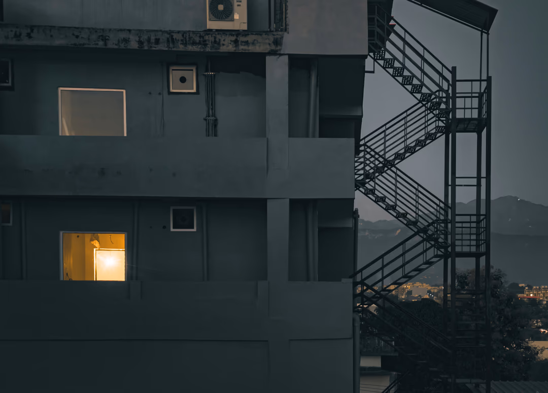 夜裡一棟公寓外牆，數十扇窗戶多半漆黑，只有一扇亮著暖黃燈光，象徵混合專家模型每次只喚醒極少數專家的稀疏運作方式