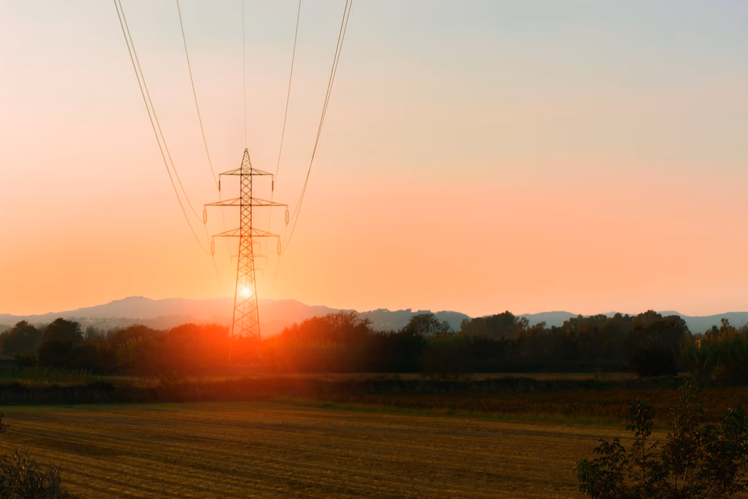 日落時分曠野上的高壓輸電鐵塔與電線，象徵電力從電網送到廠區之前，用電端完全看不見的那一段