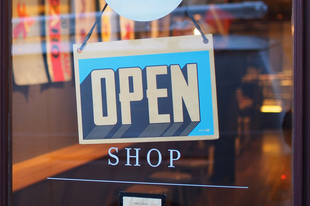 店門玻璃上掛著藍底白字的 OPEN 招牌，象徵網站永遠對外開著，但走進來的訪客不一定是人