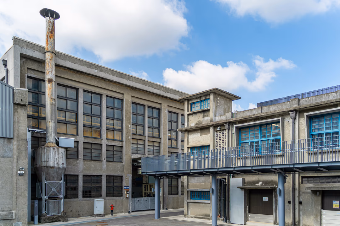 老舊水泥廠房的外觀與煙囪，大面格狀窗戶沿著牆面排開，象徵廠房、設備與庫存都會隨著時間改變，保額必須跟著重估