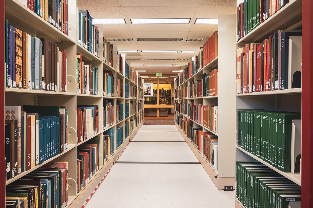 圖書館書架走道，兩側整齊排滿各色書籍，象徵企業面前同時攤開多家 AI 模型可供挑選的狀態